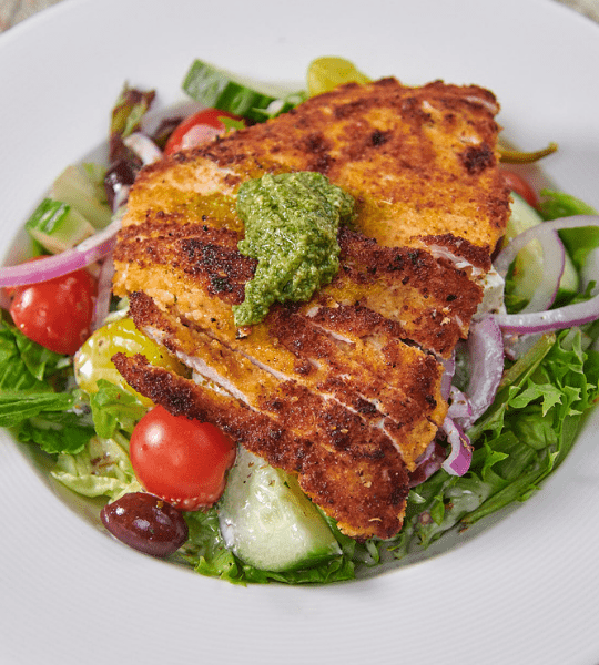 Acropolis Greek Taverna - Athenian Chicken Salad: Lightly Breaded and Pan-Fried Chicken Breast Topped with Pesto, And Served Over Lettuce Mix Topped with Pesto, Tomato, Onion, Olive, Pepperoncini, and Tossed in Acropolis Dressing. Topped with Feta Cheese and Toasted Pita Strips.