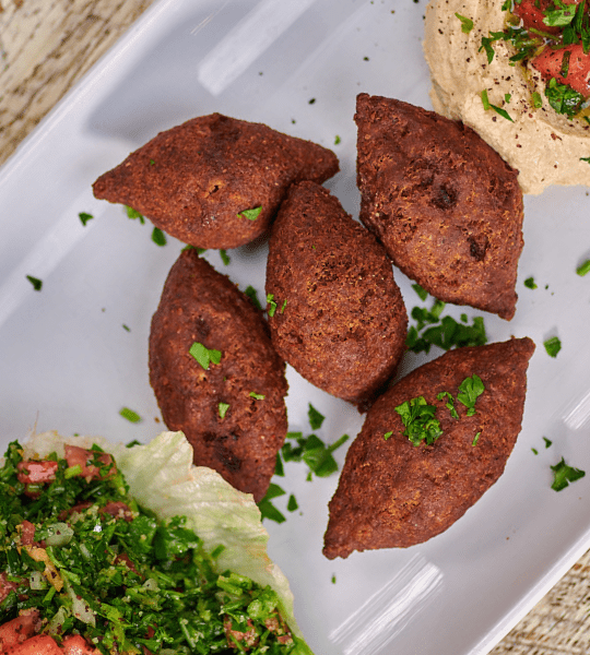 Acropolis Greek Taverna - Fried Kibbe: Dough Shell Made of Cracked Wheat and Beef, Stuffed with Sautéed Onions and Nuts. Served With Tabbouleh Salad And Hummus.