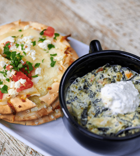 Acropolis Greek Taverna - Spinach Dip: Artichoke And Spinach Dip in a Creamy White Cheddar Cheese Topped with Tirosalata. Served with Lavash Crackers Topped with Diced Tomatoes and Cheese.