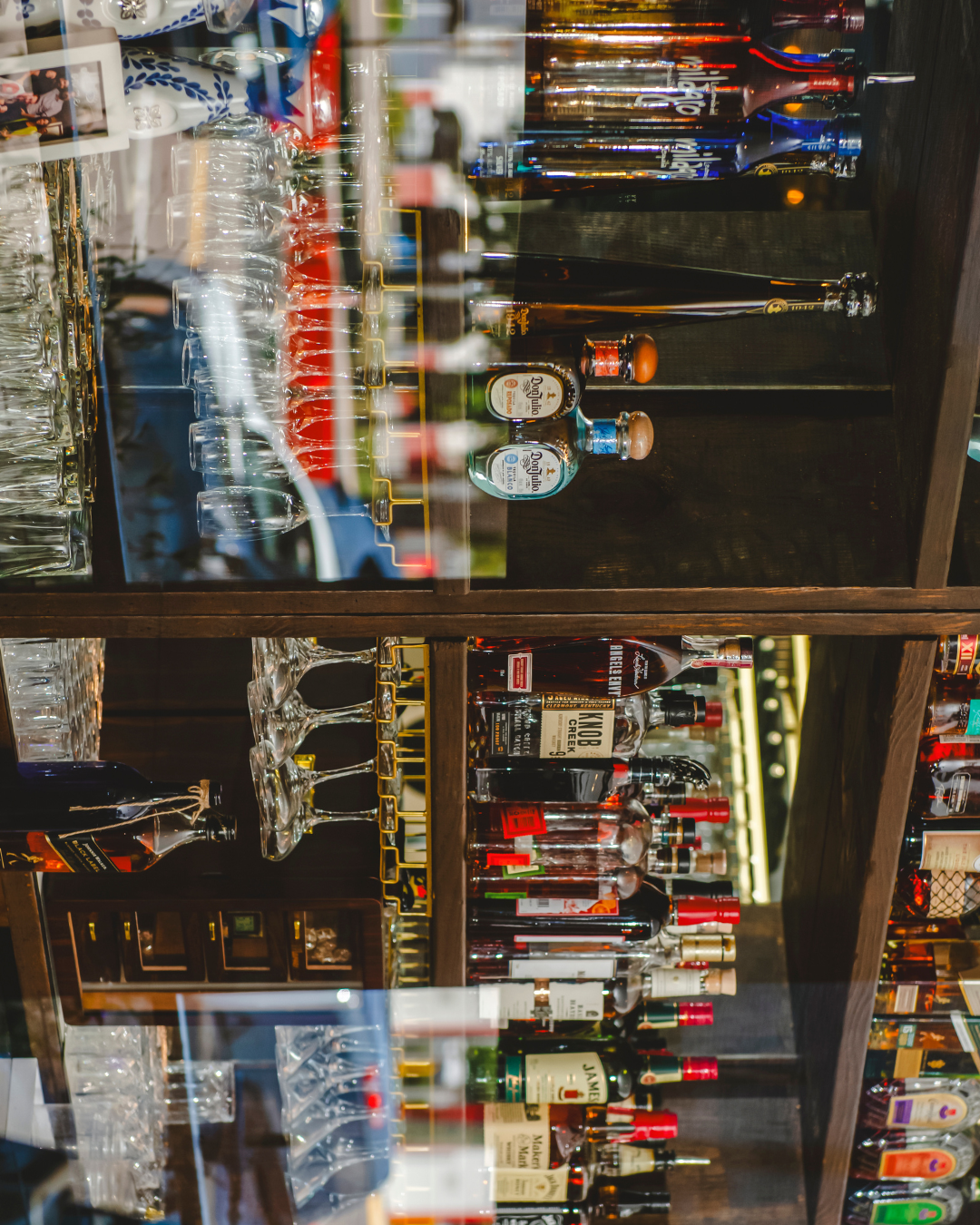 Acropolis Greek Taverna bar shelf with various spirits and glassware.